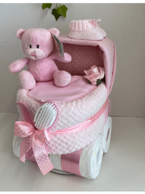 this is a pink pram nappy cake that is shaped to look like a pram, has a pink pram blanket for the body and muslin square for the hood, a pink bear sits inside with brush and comb set featured at the front