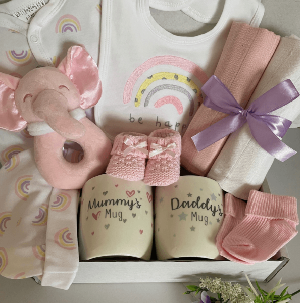 Pink rainbow baby hamper, contains baby clothing set with rainbow motif, muslin squares, booties and soft toy with mum and dad mugs