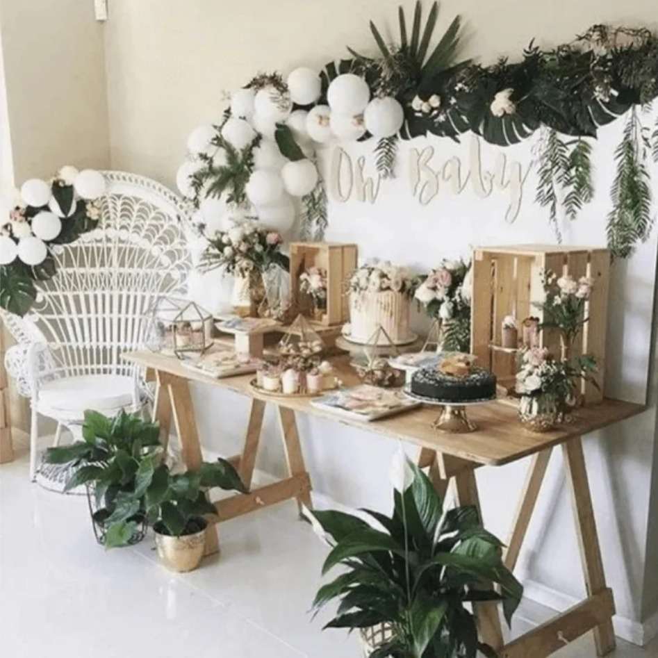 Boho Baby Shower Table setting showing a white, gold and sage green coloured set up, palm leaves, white balloons and gold cutlery that complements the theme